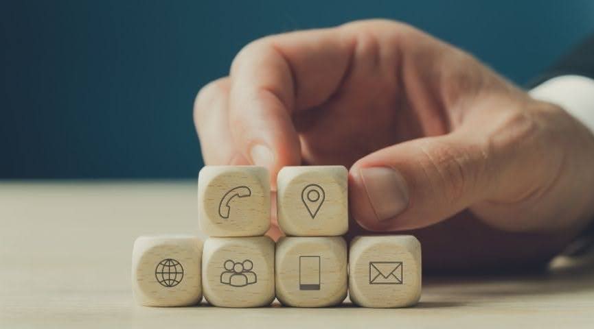 A man's hand is grabbing a small dice on a stack of other dice with communication symbols printed on them.