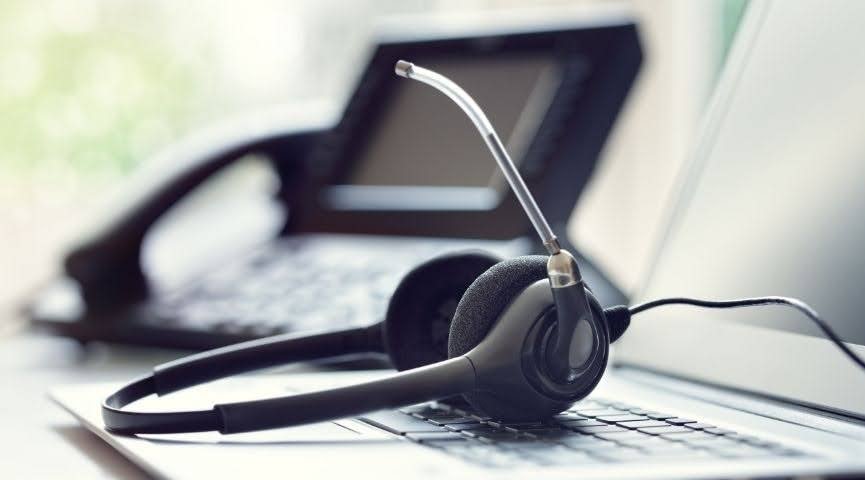 A set of headphones resting on a laptop's keyboard, with a landline phone in the background.