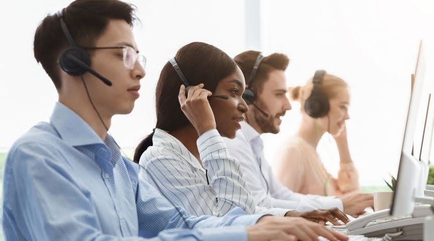 Contact centre employees wearing headsets and taking calls at a shared desk.