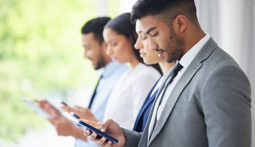 Corporate employees standing next to one another and looking at their mobile devices.